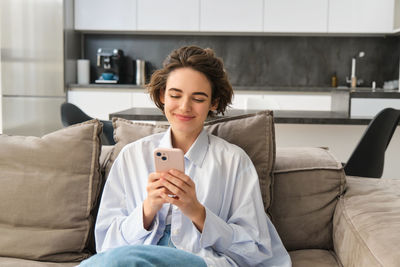 Young woman using phone while sitting on sofa at home