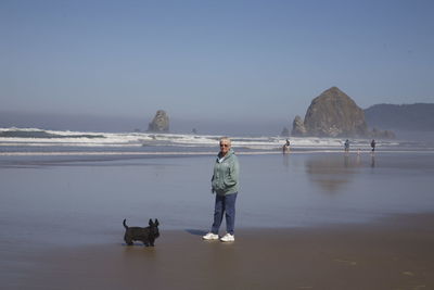 Full length of senior woman standing with dog at beach