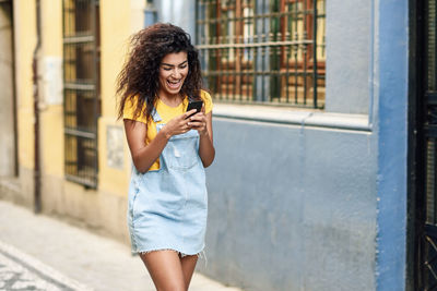 Cheerful young woman using smart phone walking on street