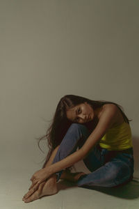 Portrait of young woman sitting against wall