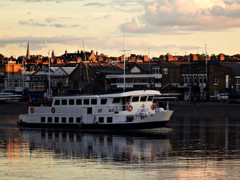 Sailboats moored on harbor by buildings against sky during sunset