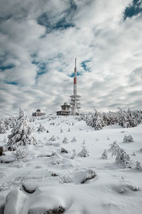 Tower on snow covered mountain against cloudy sky