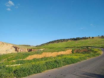 Scenic view of road amidst field against clear blue sky