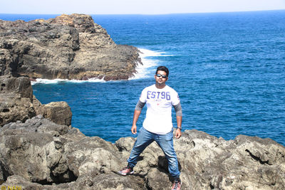 Portrait of man standing on rock by sea