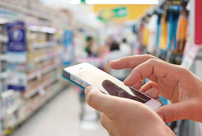 Cropped hands of woman using phone in supermarket