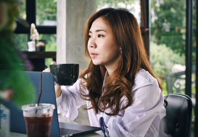 Woman with coffee cup sitting by laptop