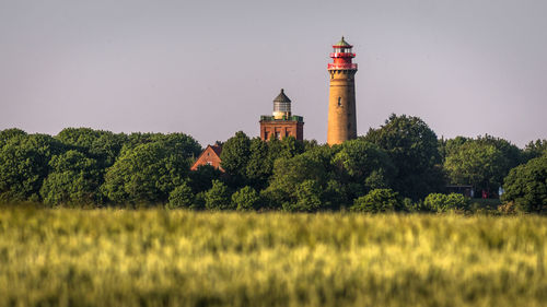 Lighthouse on field by building against sky