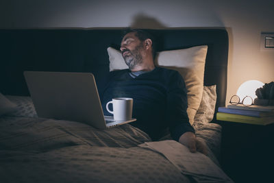 Man works with laptop lying on bed. male home working with remote office. boy sitting in bedroom 