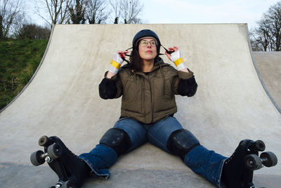 Woman with roller skates sitting on ramp in skate park