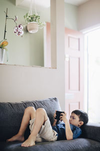 Boy using phone while lying on sofa at home