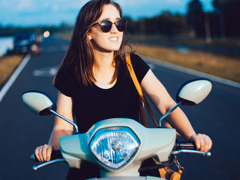 Young woman sitting on motor scooter at road