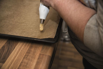 A man pushes dough through the nozzle on baking paper on a baking tray