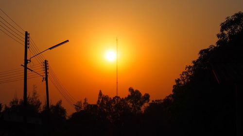 Silhouette trees and electricity pylon against sky during sunset