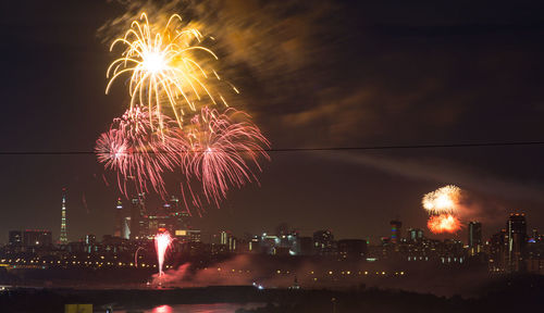 Firework display in city against sky at night