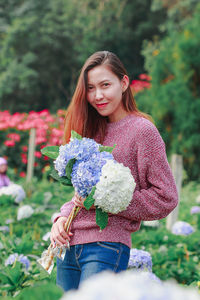 Young woman with pink flower standing against plants