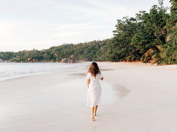 Woman in white summer dress walking on tropical sandy beach.