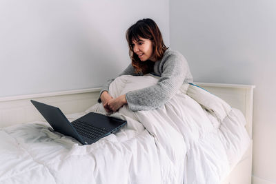 Young woman using phone while sitting on bed at home