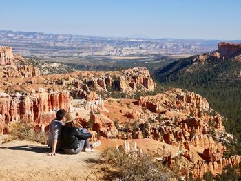 Rear view of couple sitting on rock by mountain against sky