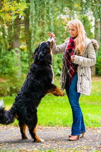 Woman playing with dog while standing on footpath in park