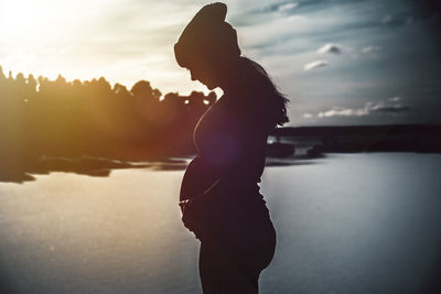 Side view of silhouette pregnant woman standing by sea during sunset