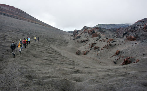 Rear view of people walking on mountain against sky