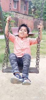 Happy boy sitting on swing at playground