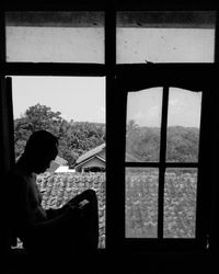 Side view of woman looking through window