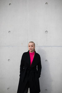 Portrait of young woman standing against wall