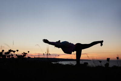 Rear view of woman exercising against sky during sunset