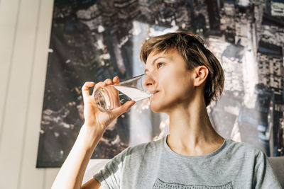 A young woman with short hair drinks water from a glass.