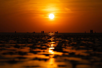 Silhouette people on sea against orange sky