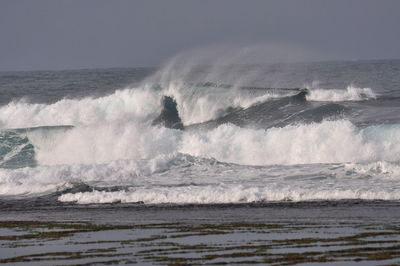 Waves splashing on shore against clear sky