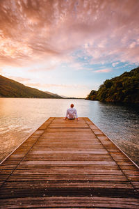 Young man sitting on the wooden jetty of lake mergozzo at dawn with colorful clouds