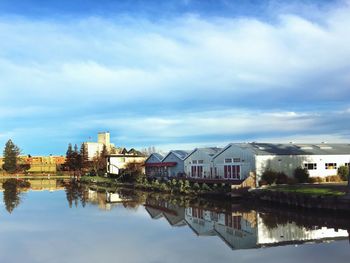 Reflection of warehouses on river against cloudy sky