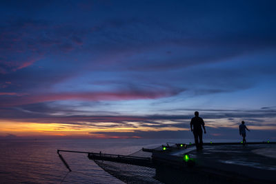 Silhouette people standing on jetty against sea during sunset