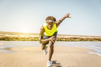 Portrait of athlete running at beach against clear sky