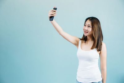 Portrait of smiling young woman photographing against white background