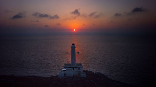 Lighthouse by sea against sky during sunset