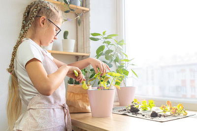 Caring for housplant coleus by a girl 10-11 years old in apron at home by window