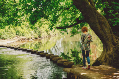 Rear view full length of woman walking on stepping stones by pond at park