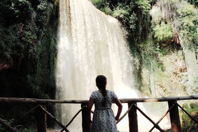 Rear view of girl standing against waterfall