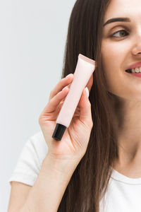 Woman with straight hair shows small tube of cosmetic product in studio closeup