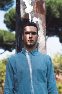 Portrait of young man standing against tree