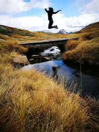 Woman jumping over river against sky