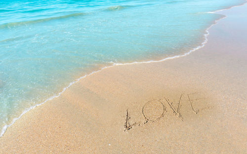 Love word hand writting letter on brown sand beach near small wave of blue water in the sea