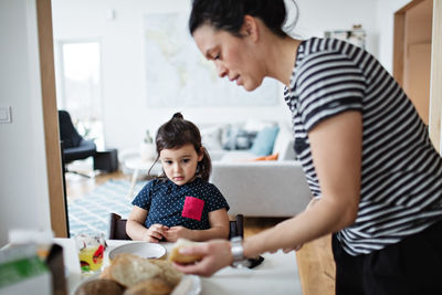 Girl looking at mother serving food on table