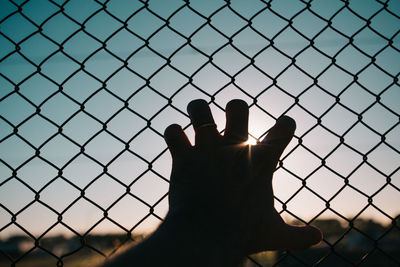 Close-up of hand against fence against sky