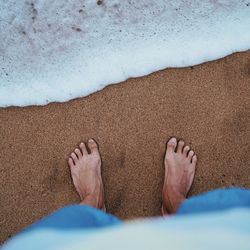 Low section of man relaxing on sand at beach