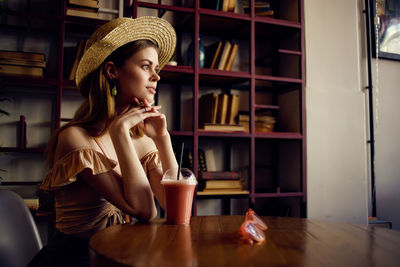 Young woman looking away while sitting on table at cafe