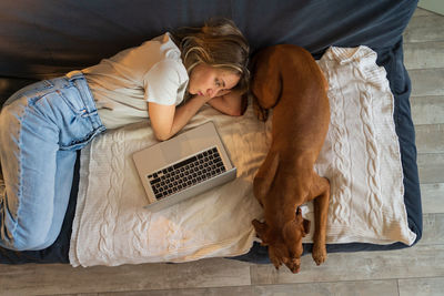 High angle view of woman with dog using laptop on sofa at home